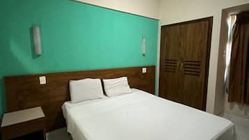 A hotel room with a large bed, a wooden headboard, a teal accent wall, a wooden wardrobe, and a nightstand.