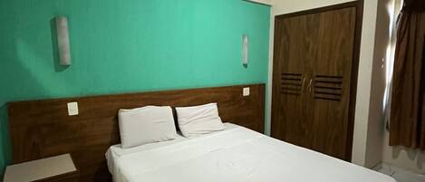Habitación de hotel con una cama grande, cabecera de madera, pared de acento color turquesa, armario de madera y mesita de noche.