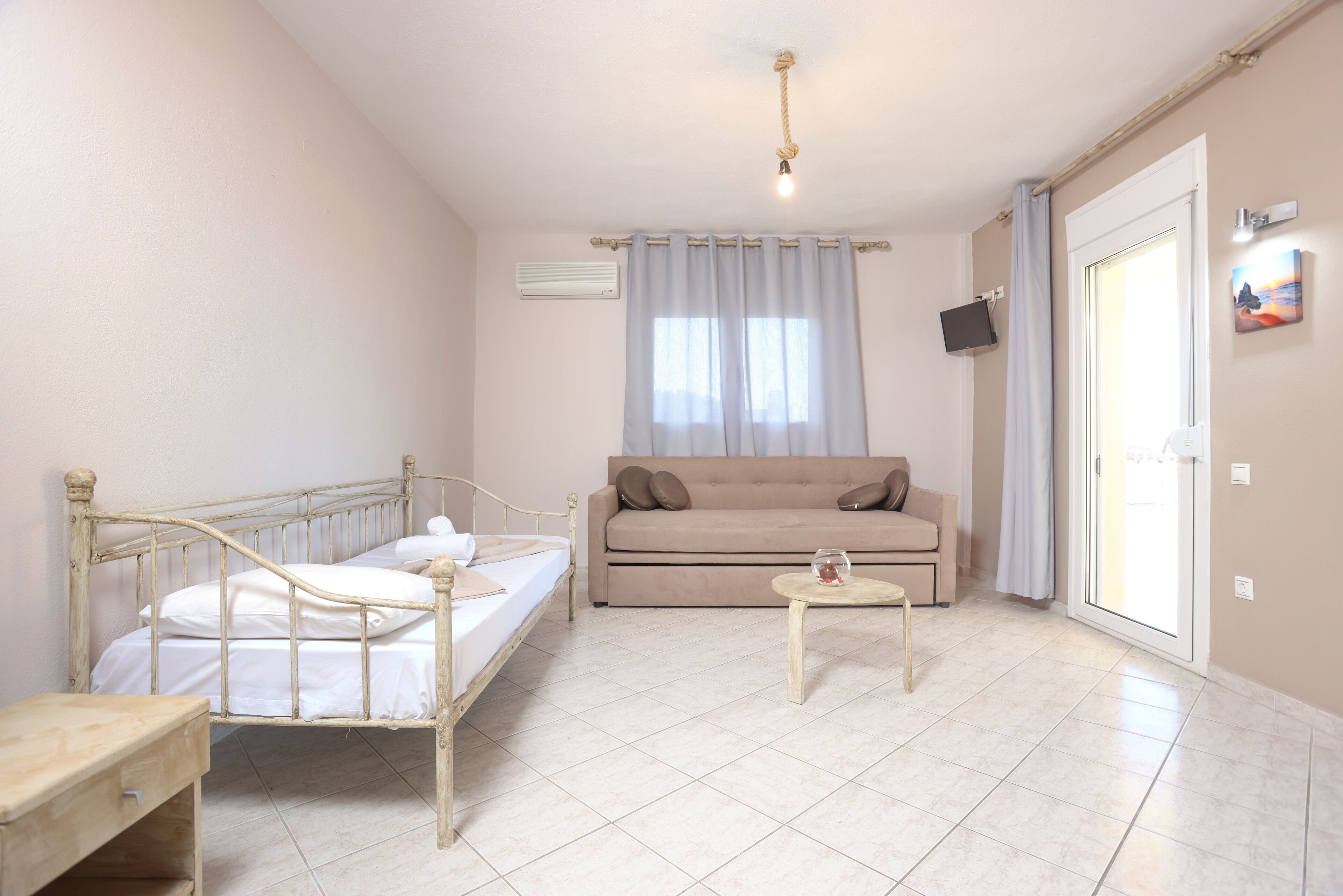A room with a bed, a sofa, a small table, and a TV on the wall.
