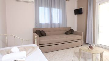 Ein Hotelzimmer mit einem Bett, einem Sofa, einem kleinen Tisch mit einer Glasschale und einem an der Wand befestigten Fernseher.