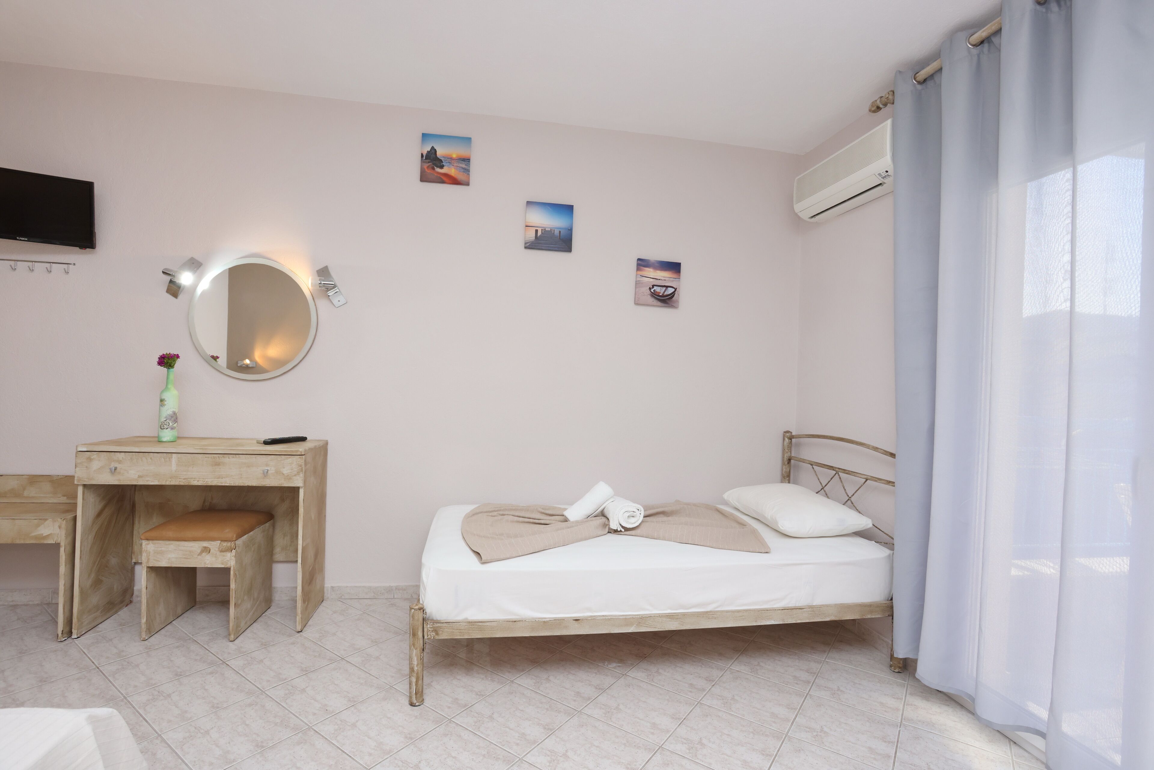 Un dormitorio con cama, escritorio, silla, espejo y aire acondicionado instalado en la pared.