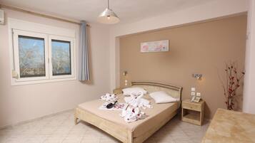 A bedroom with a bed, bedside table, nightstand, and a window with curtains.