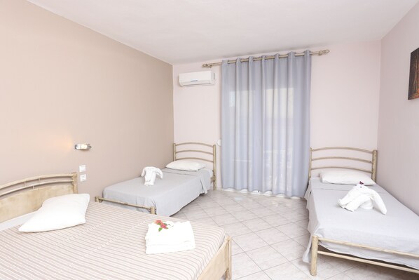 A room with two single beds, a window with a curtain, an air conditioning unit, and a wall-mounted light fixture. - Summer Dream Hotel (Kassandra)