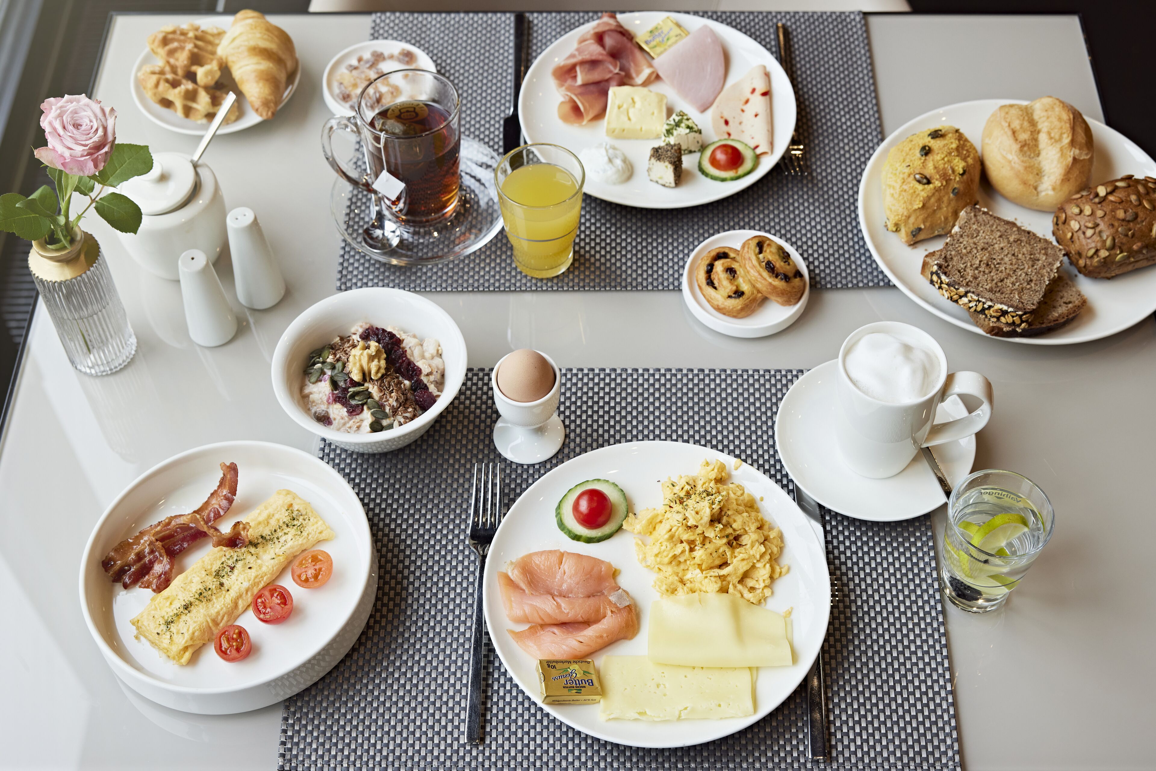 Un desayuno servido con varios platos, entre ellos huevos, tocino y bollería, sobre una mesa con mantel individual.