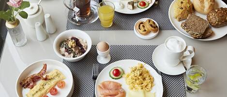 Un desayuno servido con varios platos, entre ellos huevos, tocino y bollería, sobre una mesa con mantel individual.