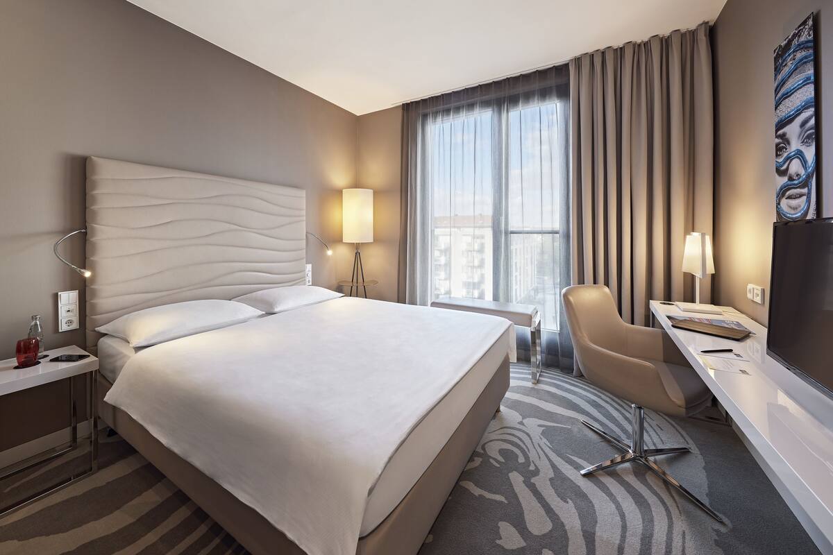 Una habitación de hotel moderna con una cama grande, un escritorio, una silla y un televisor.