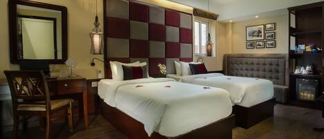 A hotel room with two beds, a desk, a chair, a mirror, and a bedside table.