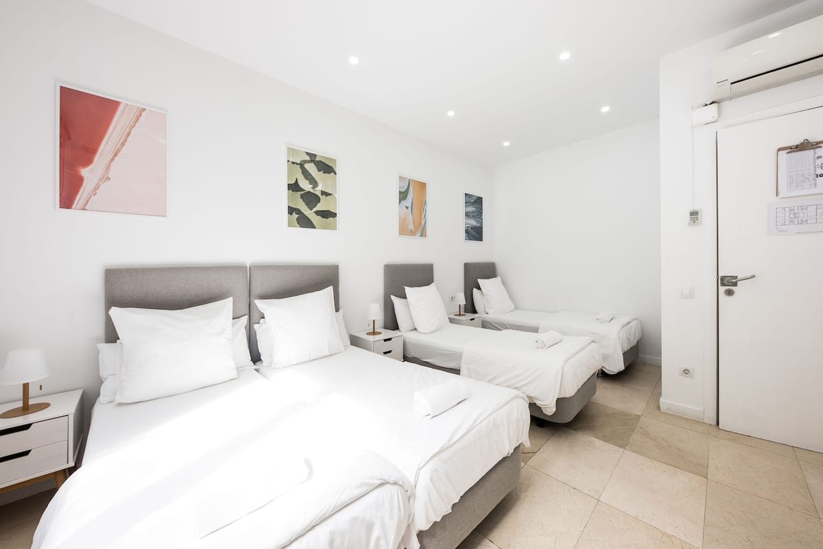 A hotel room with three beds, white bedding, and artwork on the walls.