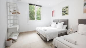 Un dormitorio moderno con dos camas, un armario blanco y un ventanal amplio.