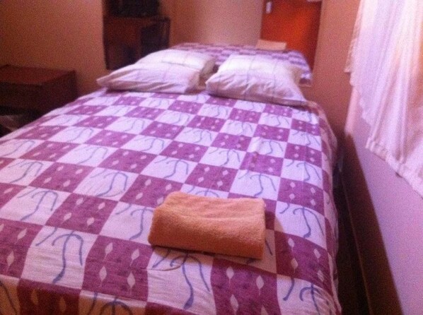 A hotel room with a bed covered in a purple and white checkered bedspread, two pillows, and a folded towel on the bed. - Hospedaje Yemaya (Nazca)