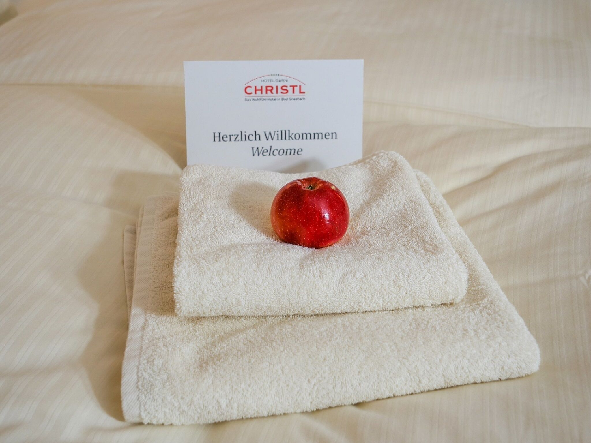 Tarjeta de bienvenida del hotel con una manzana roja sobre una toalla doblada.