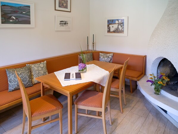 A cozy living room with a wooden table, matching chairs, a bench, and a fireplace. - Hotel Garni Christl (Bad Griesbach im Rottal)