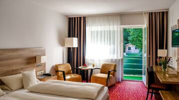 Habitación de hotel con cama, dos sillones, una mesita con un florero y un escritorio con lámpara.