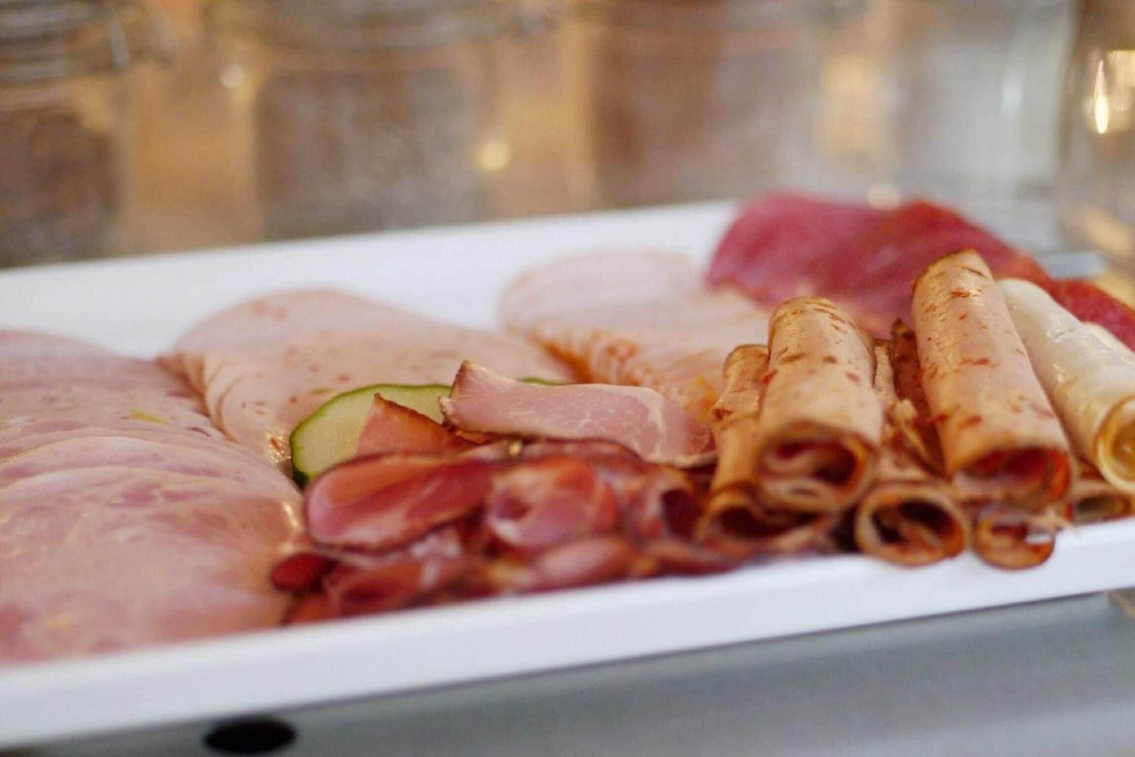 A variety of meats including sliced ham, bacon, and rolled meat on a white plate.