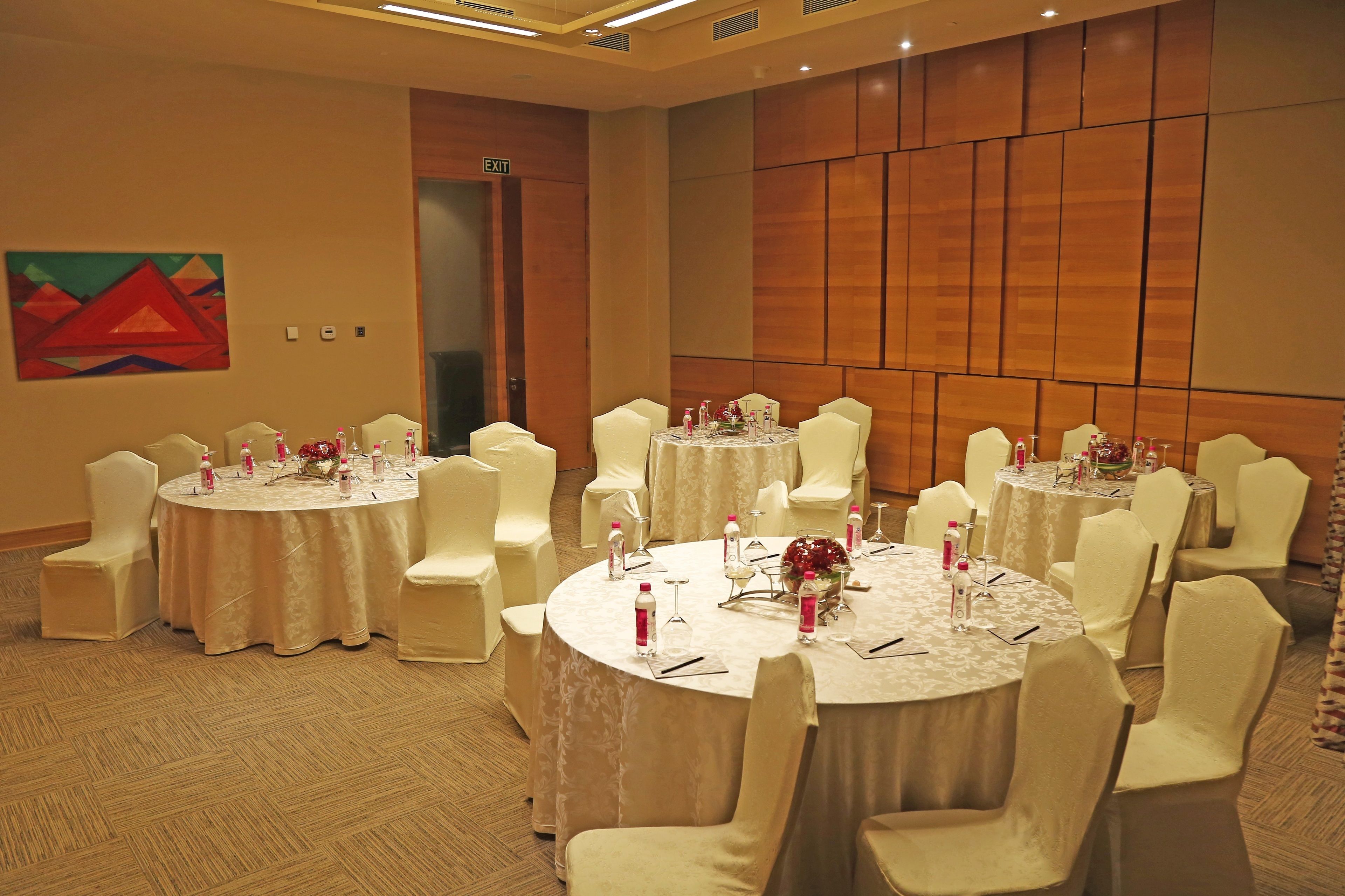 A conference room with round tables, white chairs, and a wooden panel wall.