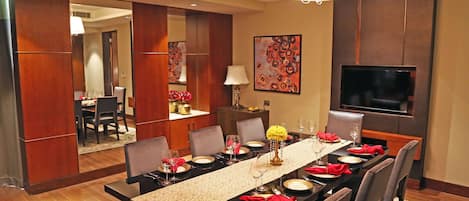 A dining area with a long table set for six, a television mounted on the wall, and a mirror reflecting the room.