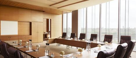 A conference room with a long table, multiple chairs, and large windows offering a view of the city.