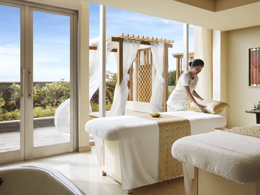Une salle de spa équipée de deux tables de massage, d’une grande fenêtre et offrant une vue sur la verdure.