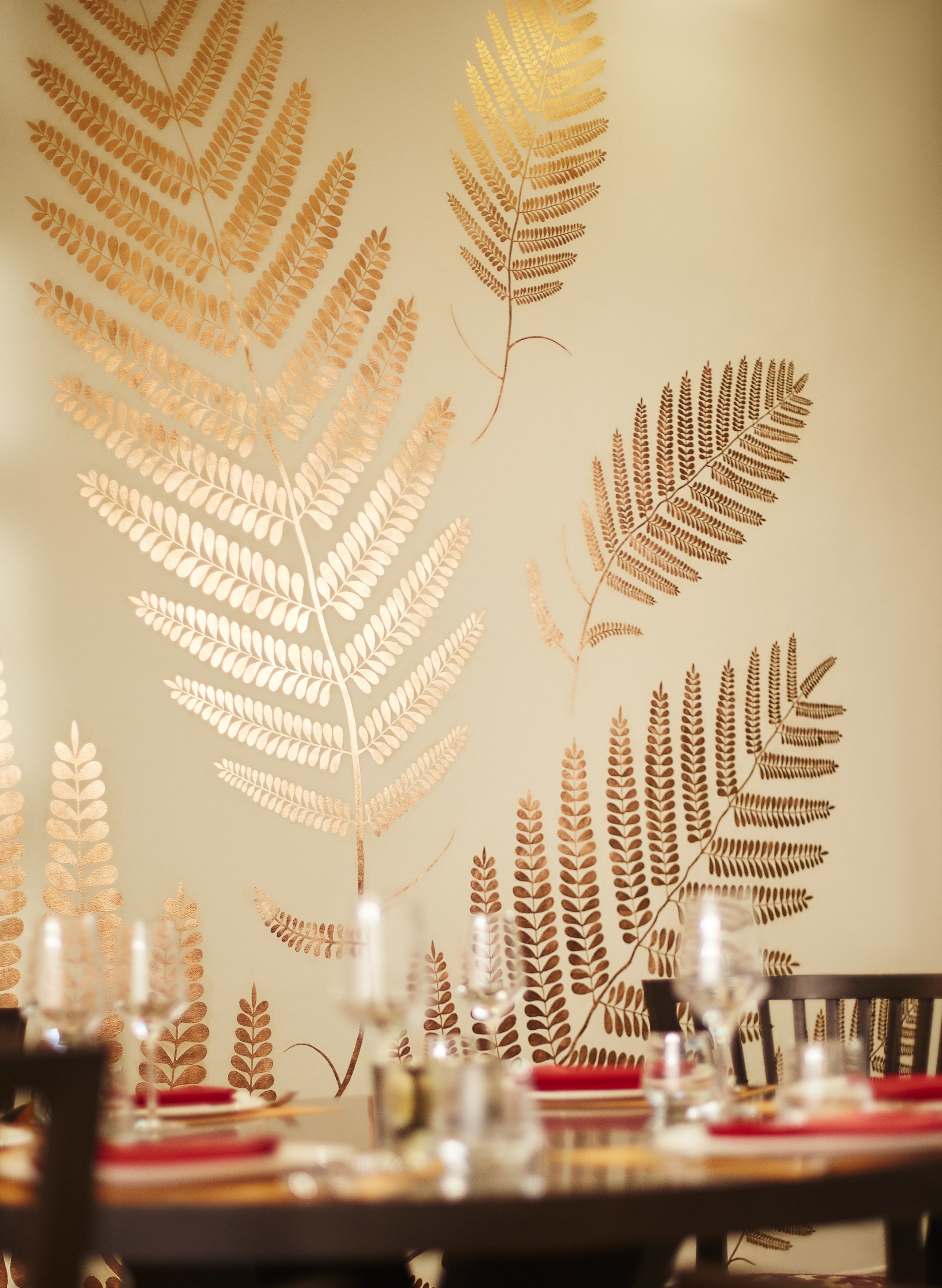A dining table with a decorative fern leaf pattern on the wall behind it.