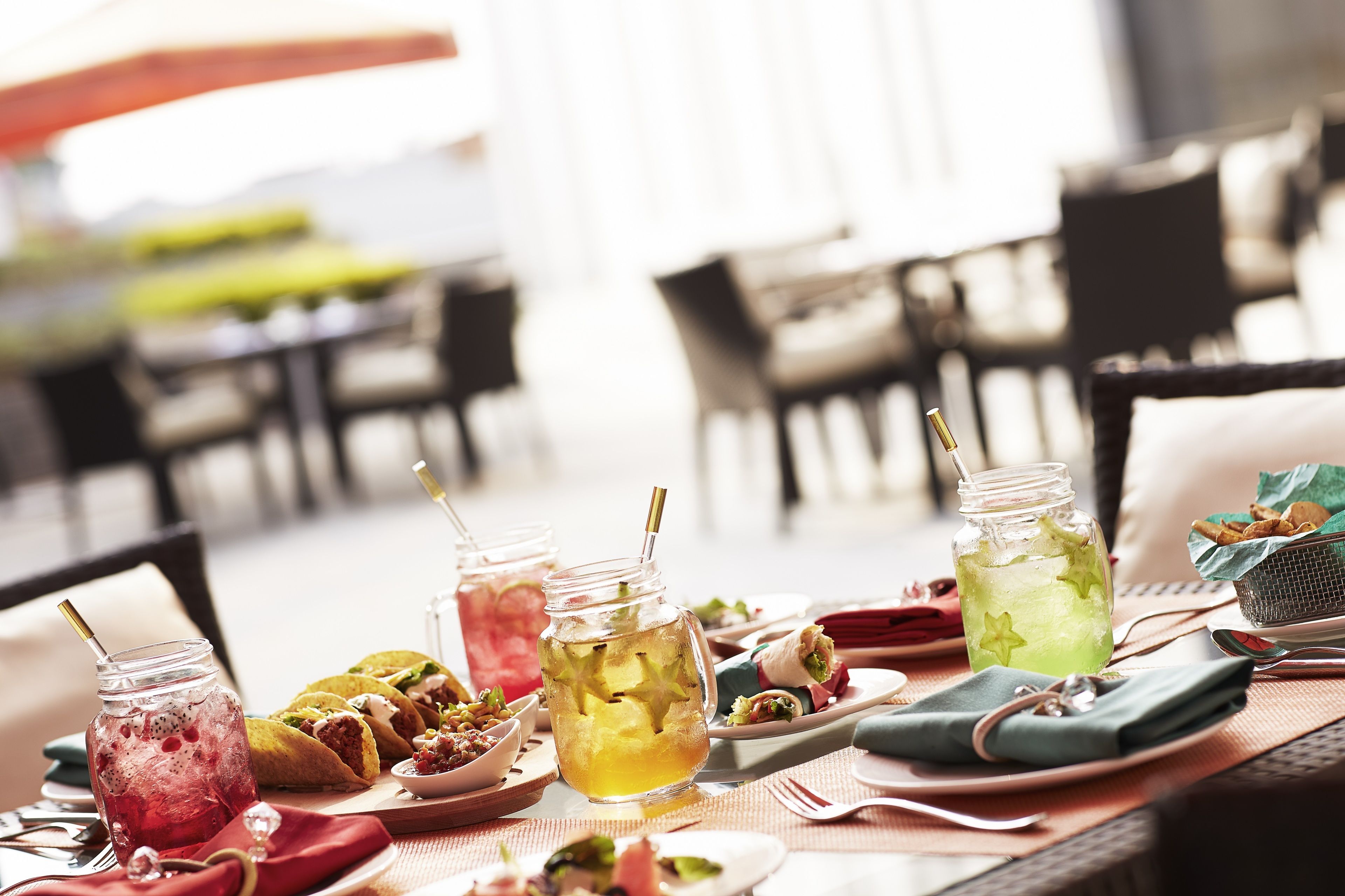 A dining table with various food items and drinks, including tacos, a green beverage, and a pink drink, in a restaurant setting.