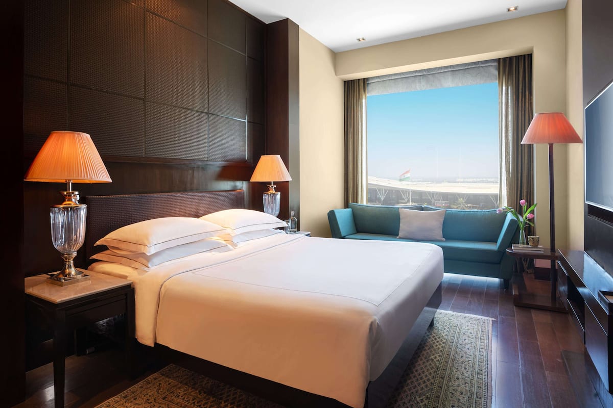A hotel room with a large bed, two bedside lamps, a sofa, a TV, and a window with a view.