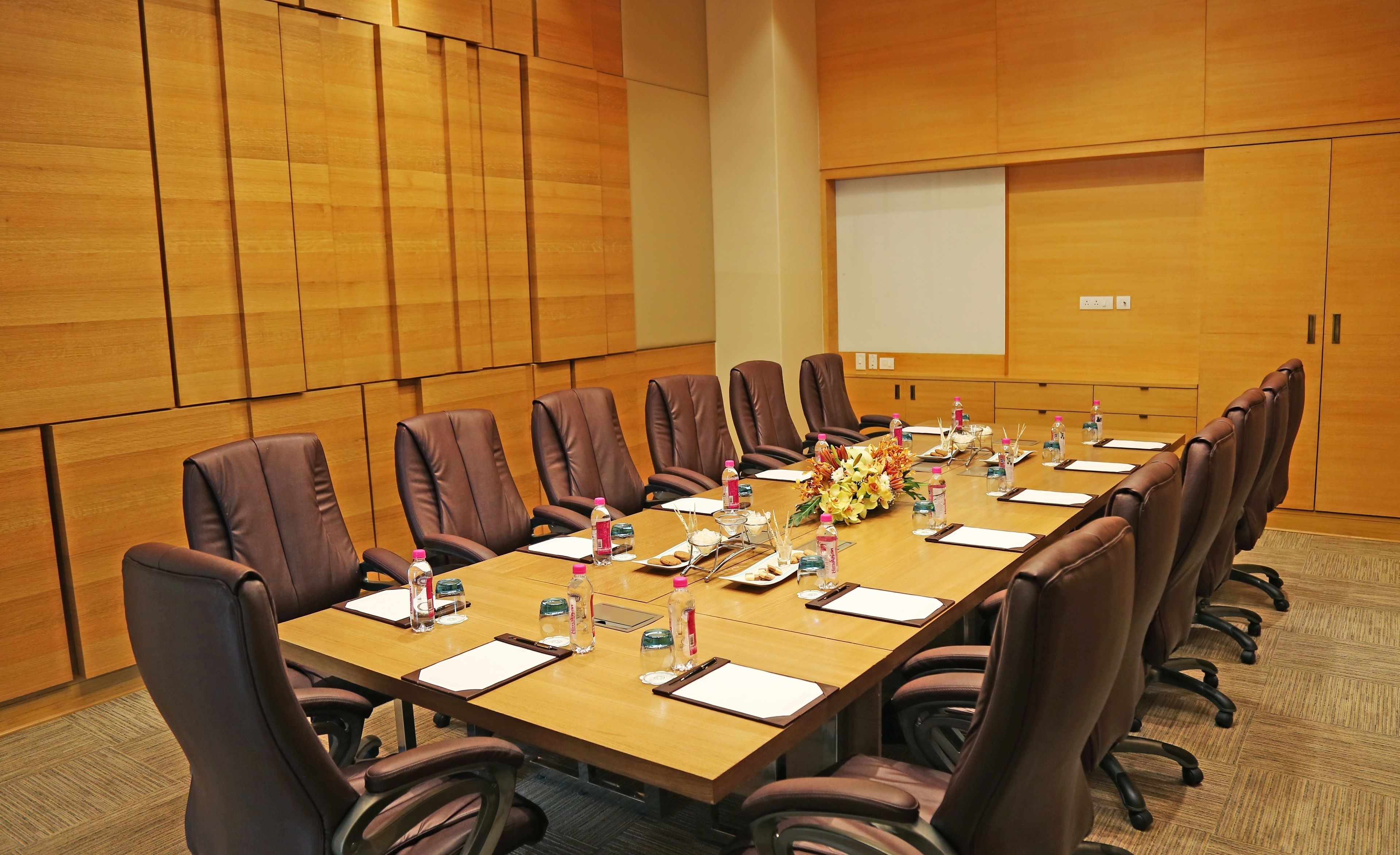 A conference room with a long table, brown leather chairs, water bottles, and a projector screen.