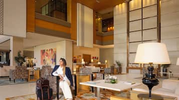 A spacious lobby with a modern design, featuring a seating area with sofas and armchairs, a reception desk, and a large window providing a view of the interior.