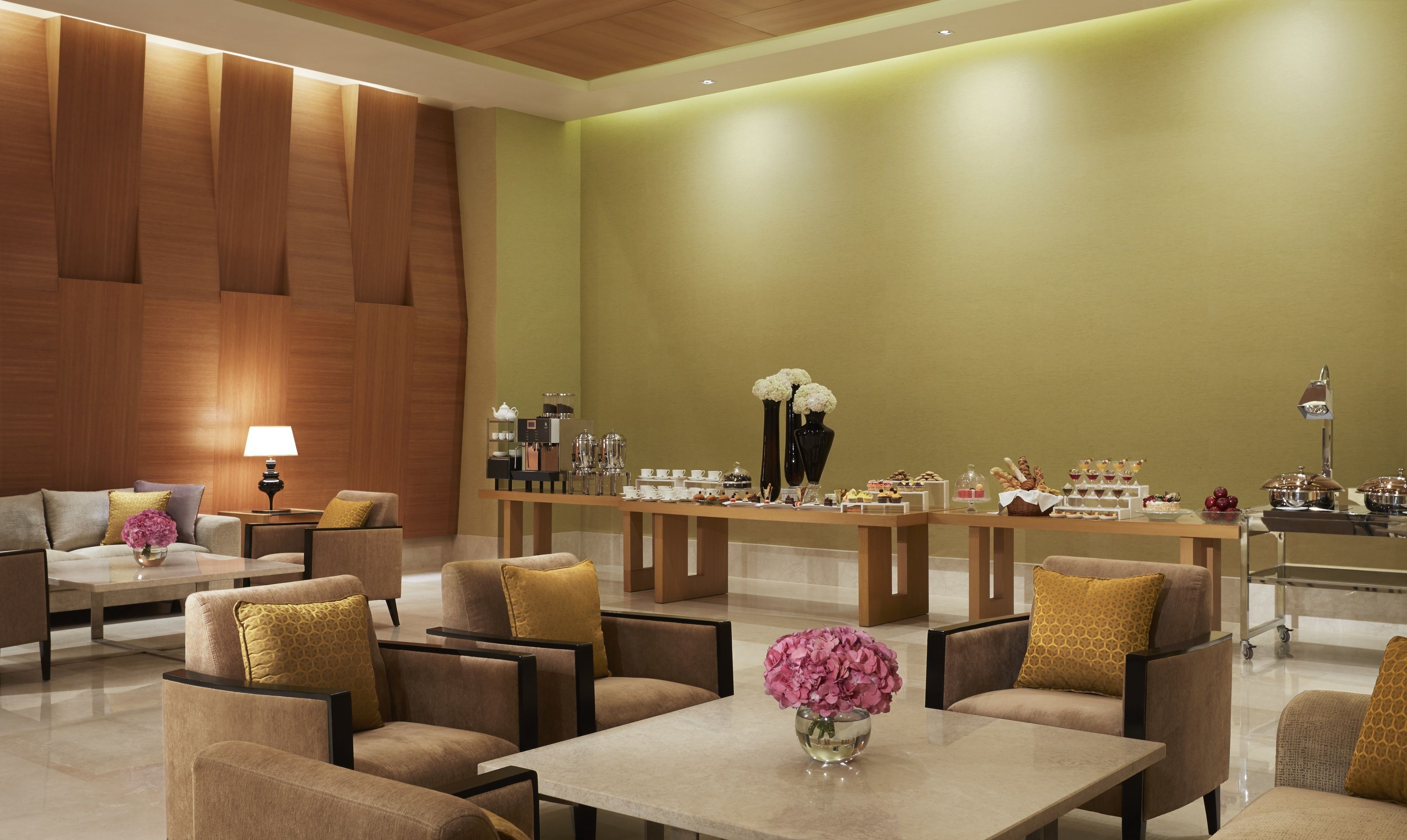 A modern lobby with a green wall, wooden paneling, and a buffet area with various food items.