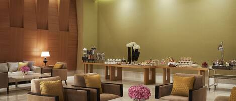 A modern lobby with a green wall, wooden paneling, and a buffet area with various food items.