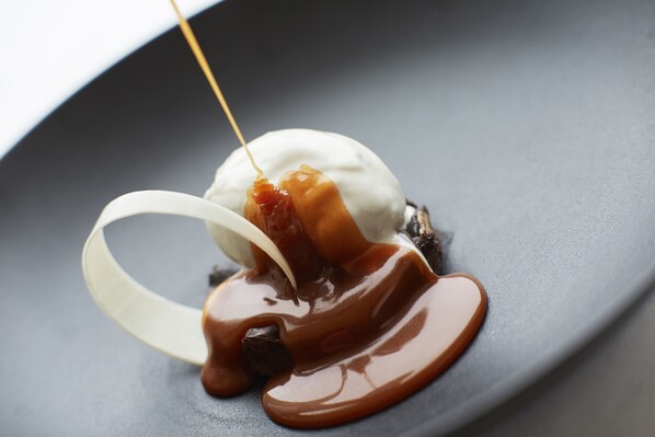 A dessert with a scoop of ice cream, caramel sauce, and a piece of fruit on a plate. - Taj Bangalore (Devanahalli)