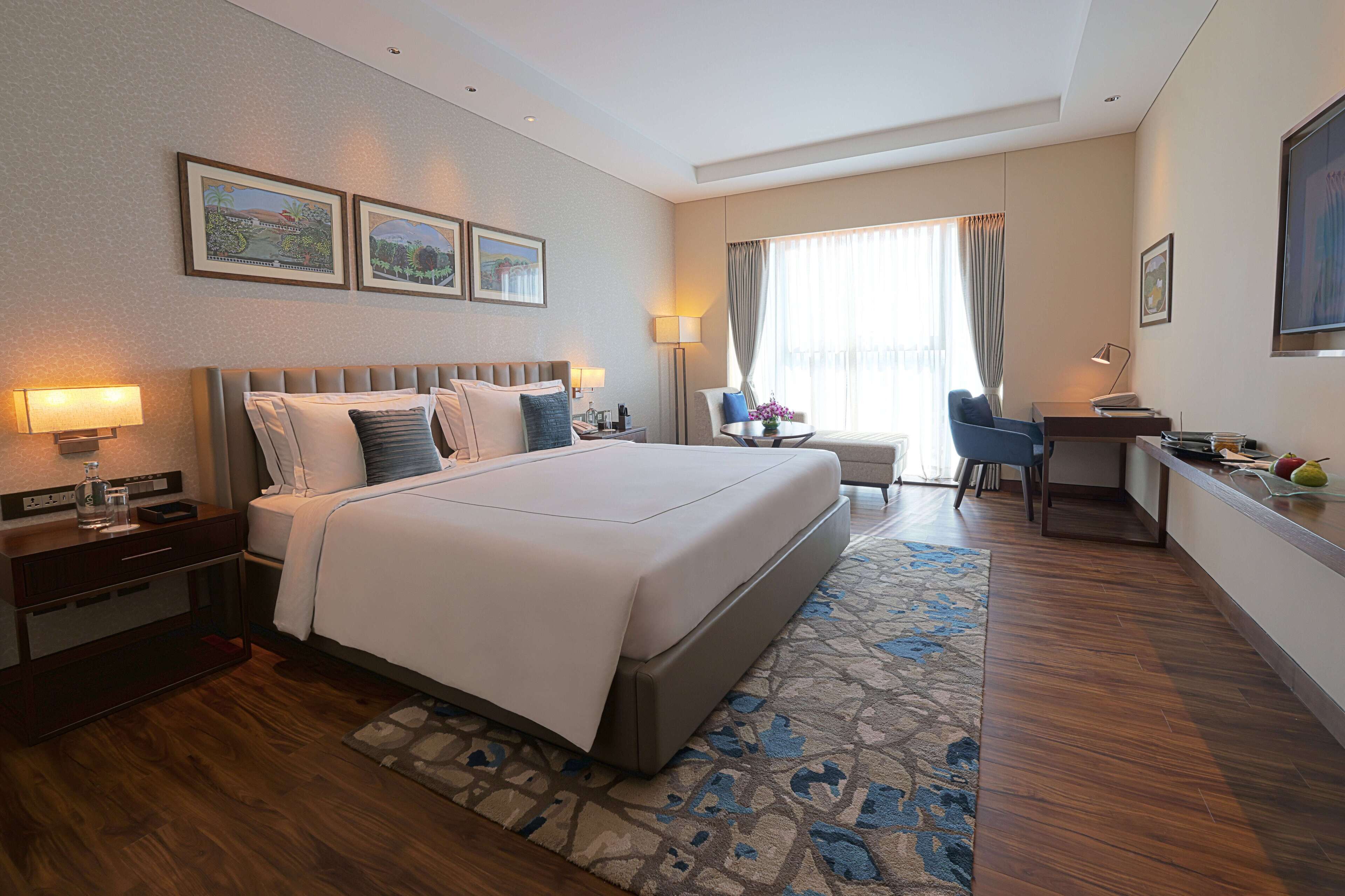 A hotel room with a large bed, a desk, a chair, and a window with curtains.