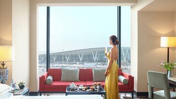 A hotel room with a large window, a red sofa, a dining table with breakfast, and a bed.