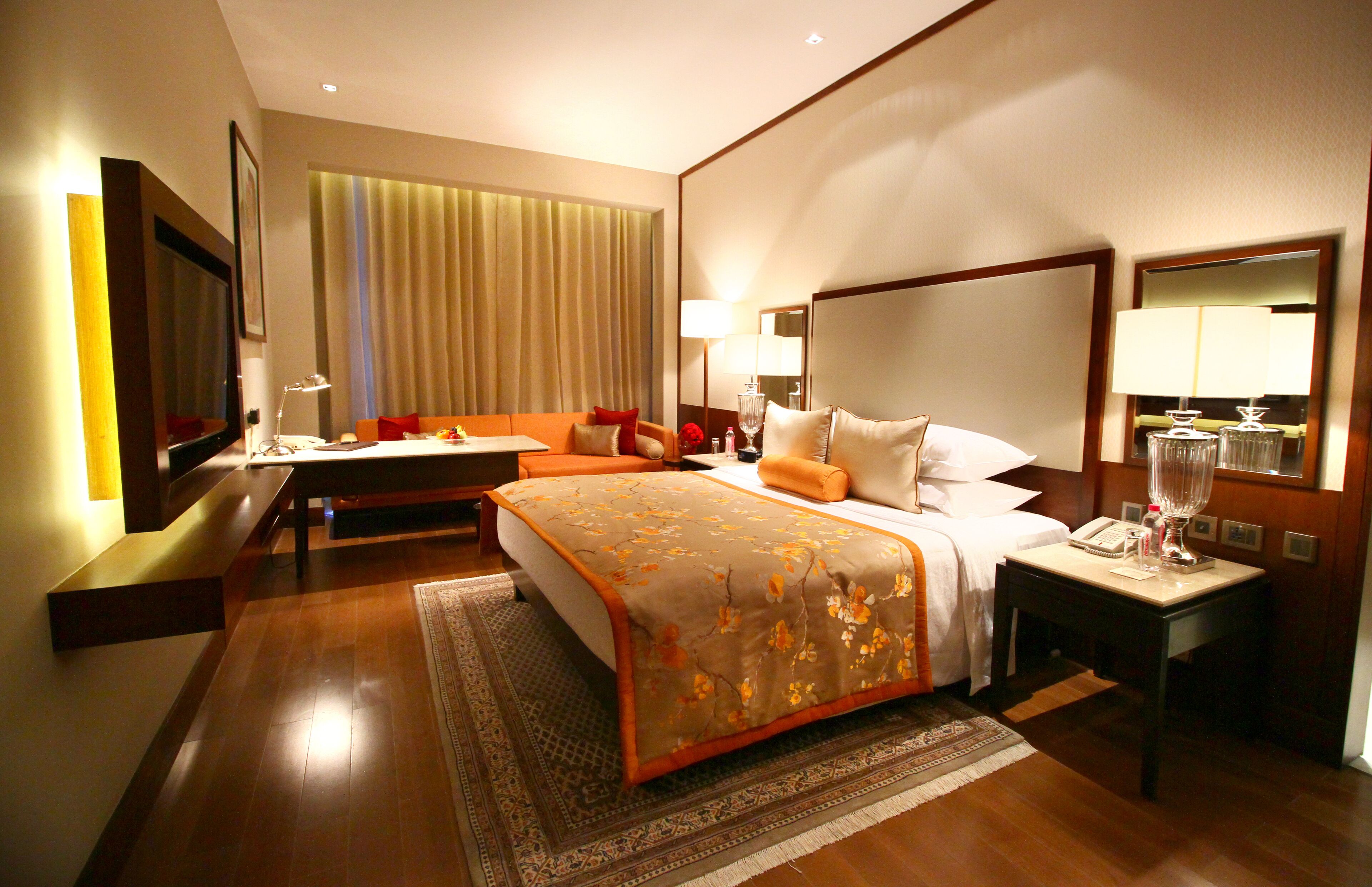 A hotel room with a large bed, a desk, a chair, a TV, and a window with curtains.