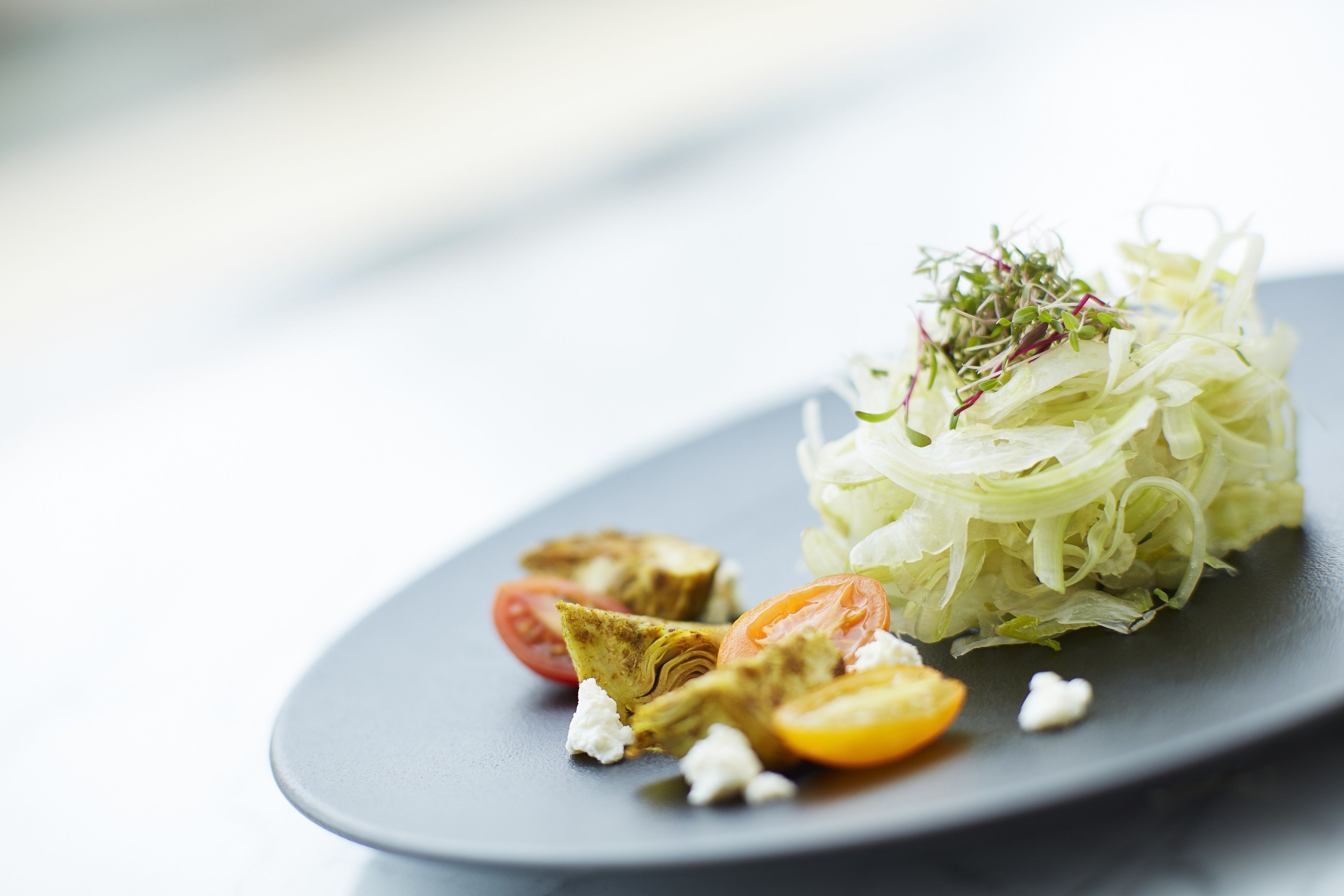 Un plato con ensalada de lechuga rallada, tomates cherry, corazones de alcachofa y queso desmenuzado.