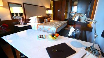 A hotel room with a bed, bedside tables, a desk with a laptop, a fruit bowl, and a bottle of champagne.