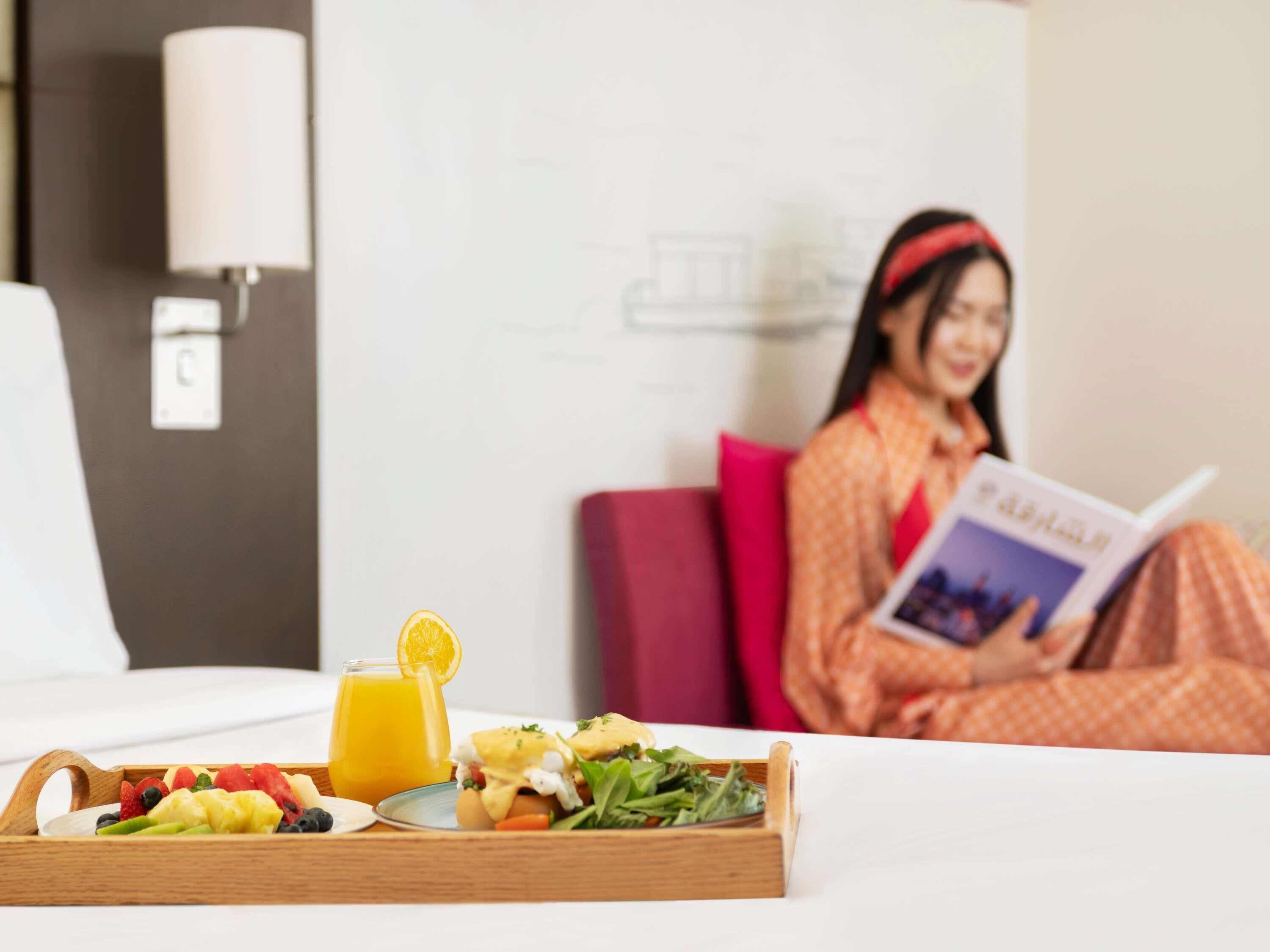 Un vassoio della colazione con frutta, un bicchiere di succo d'arancia e un panino su un letto in una camera d'hotel.