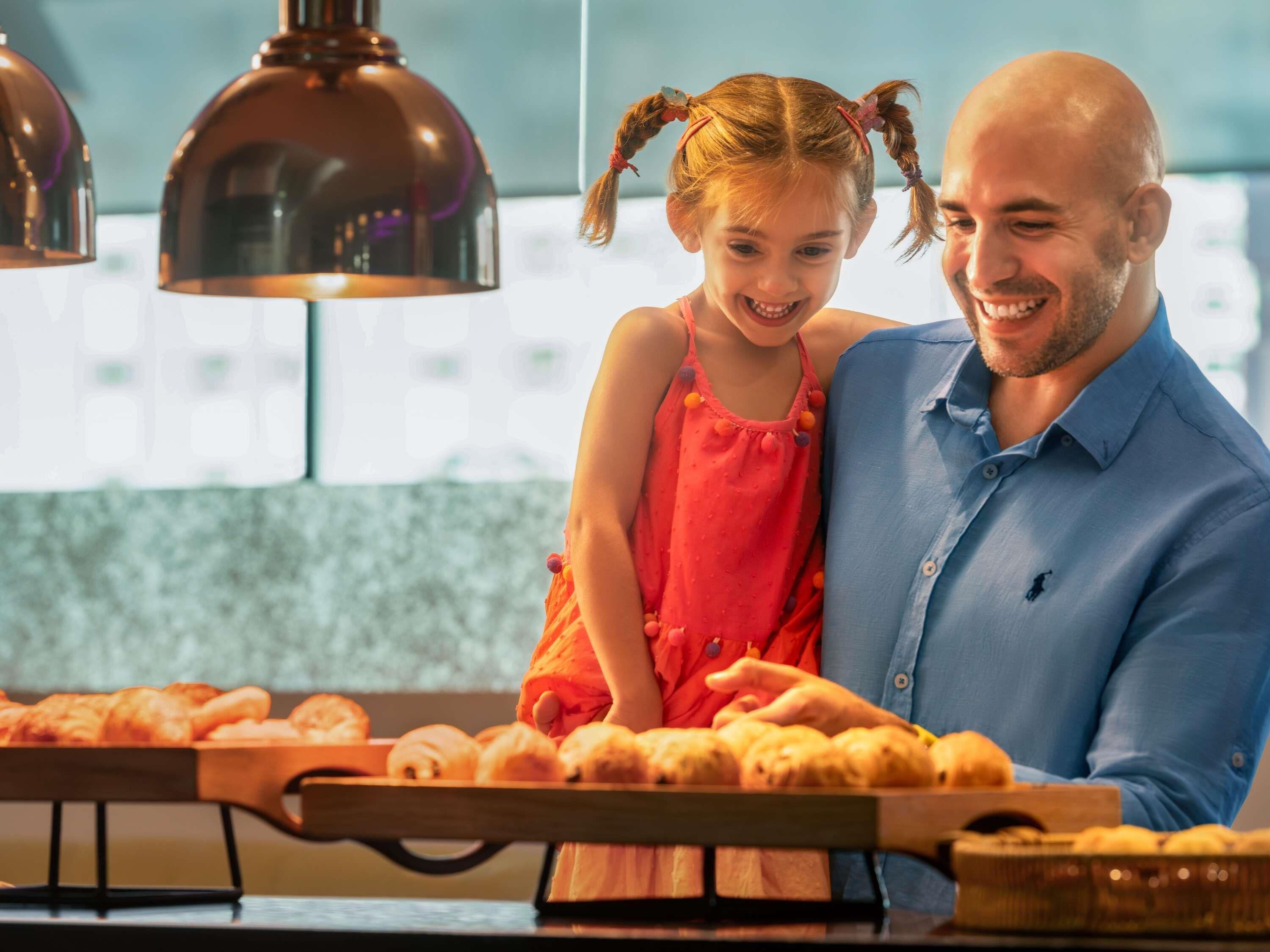 A man and a young girl in a kitchen with pastries on the counter.