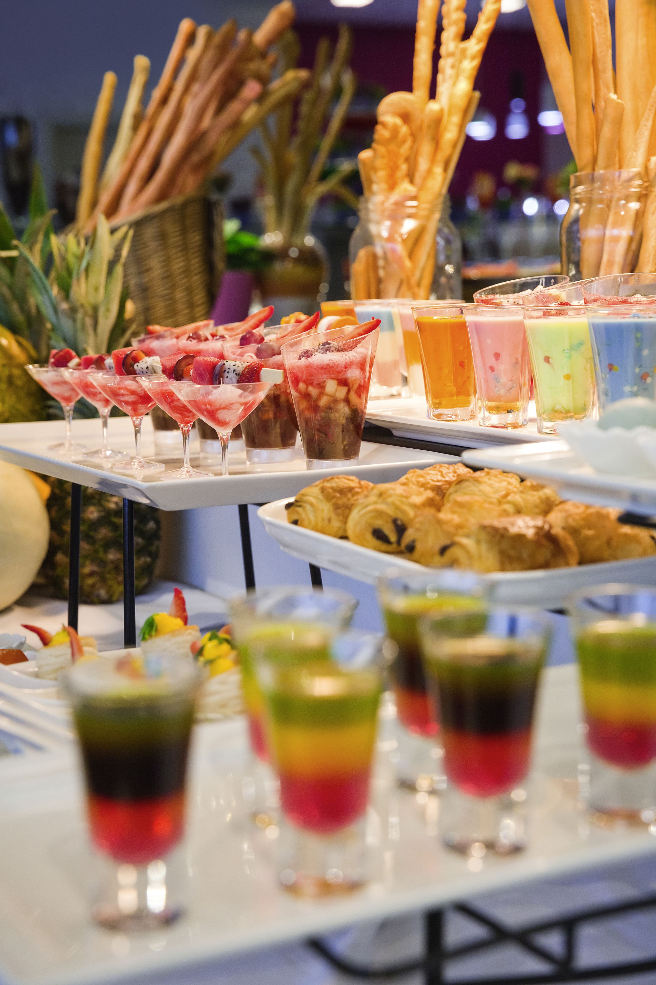A buffet table with various food items and drinks, including pastries, fruits, and colorful beverages.