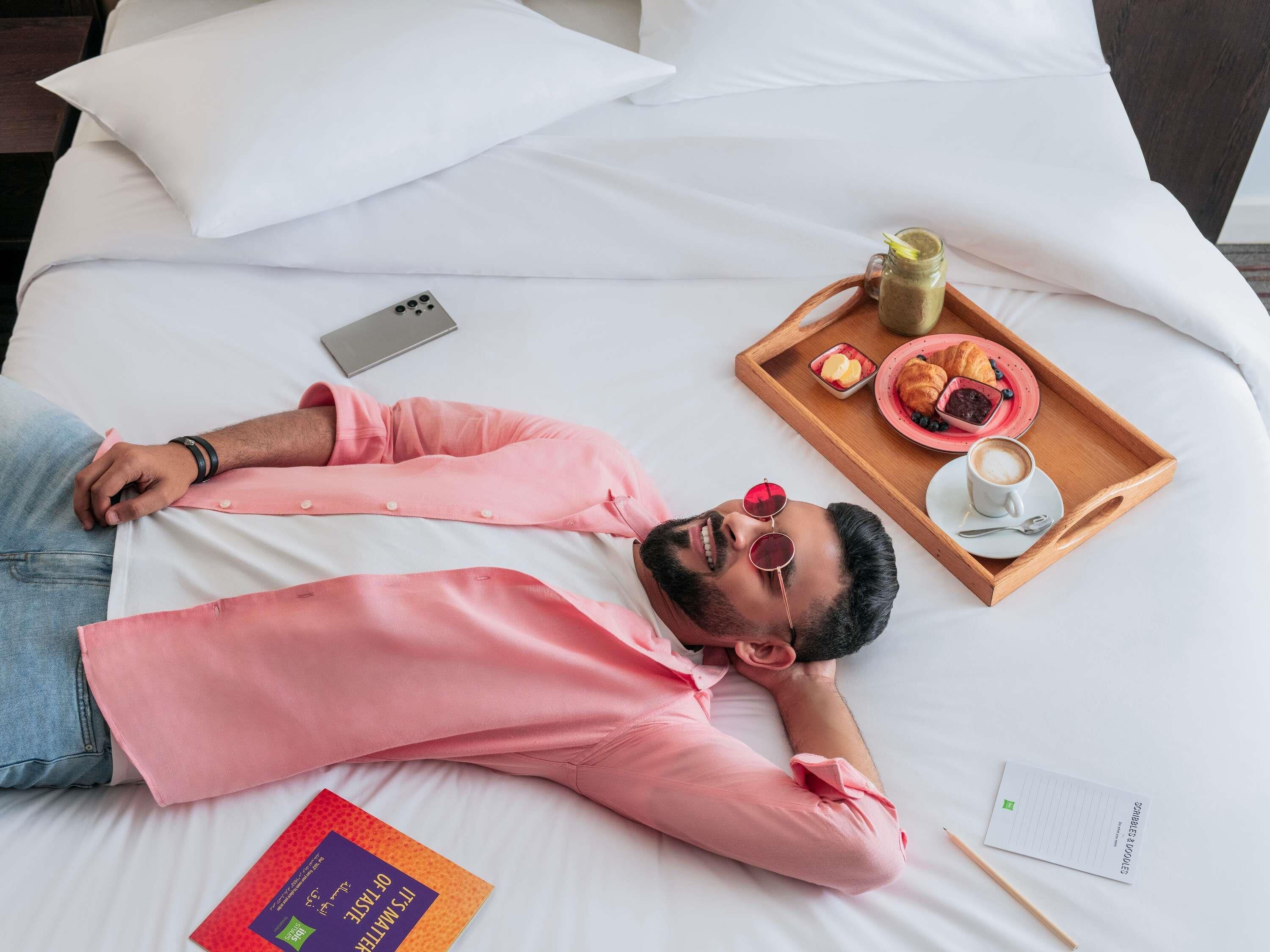 A person lying on a bed with a tray of food and a book beside them.