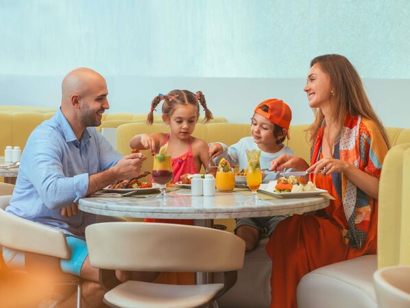 A family dining at a round table in a brightly lit room with yellow seating.