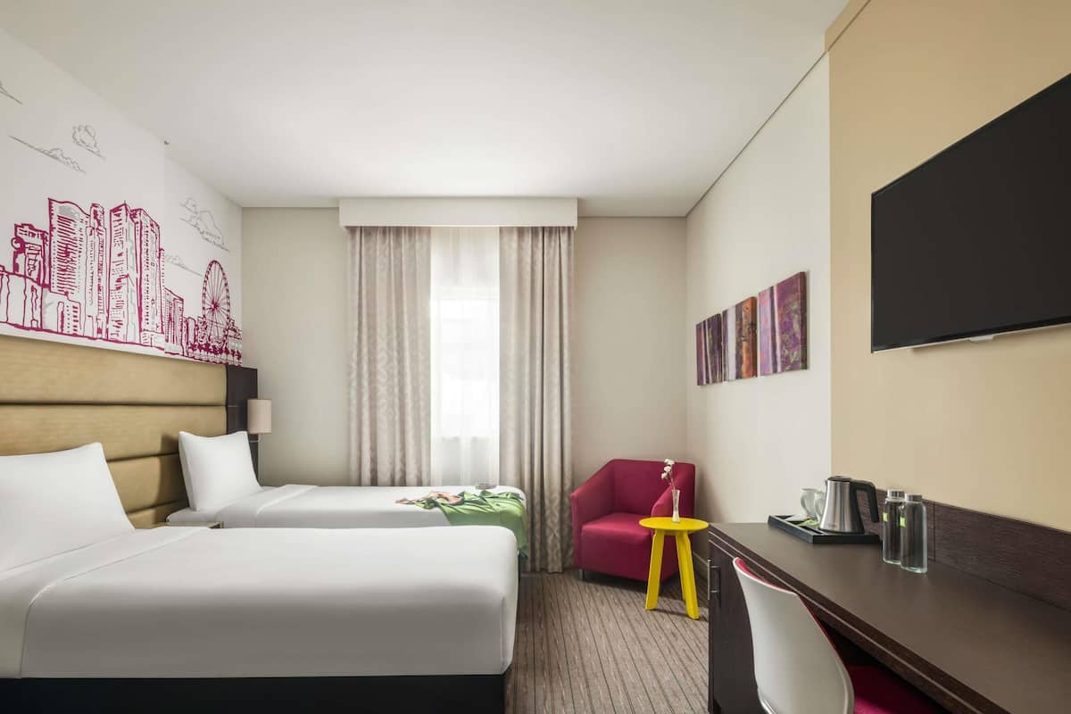 Une chambre d’hôtel avec deux lits, un bureau, une chaise, une télévision et une fenêtre avec des rideaux.