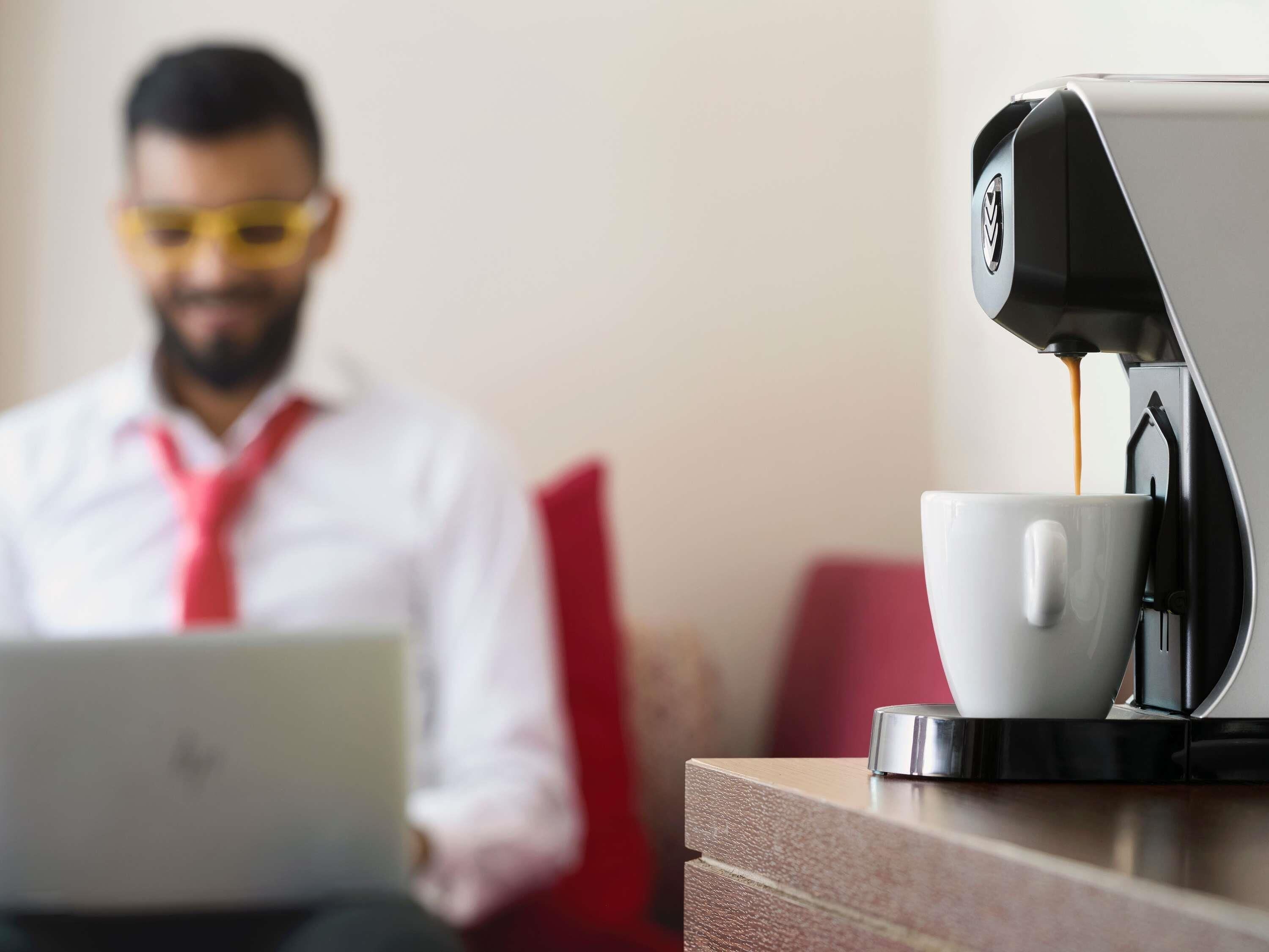 A person using a laptop with a coffee machine in the foreground.