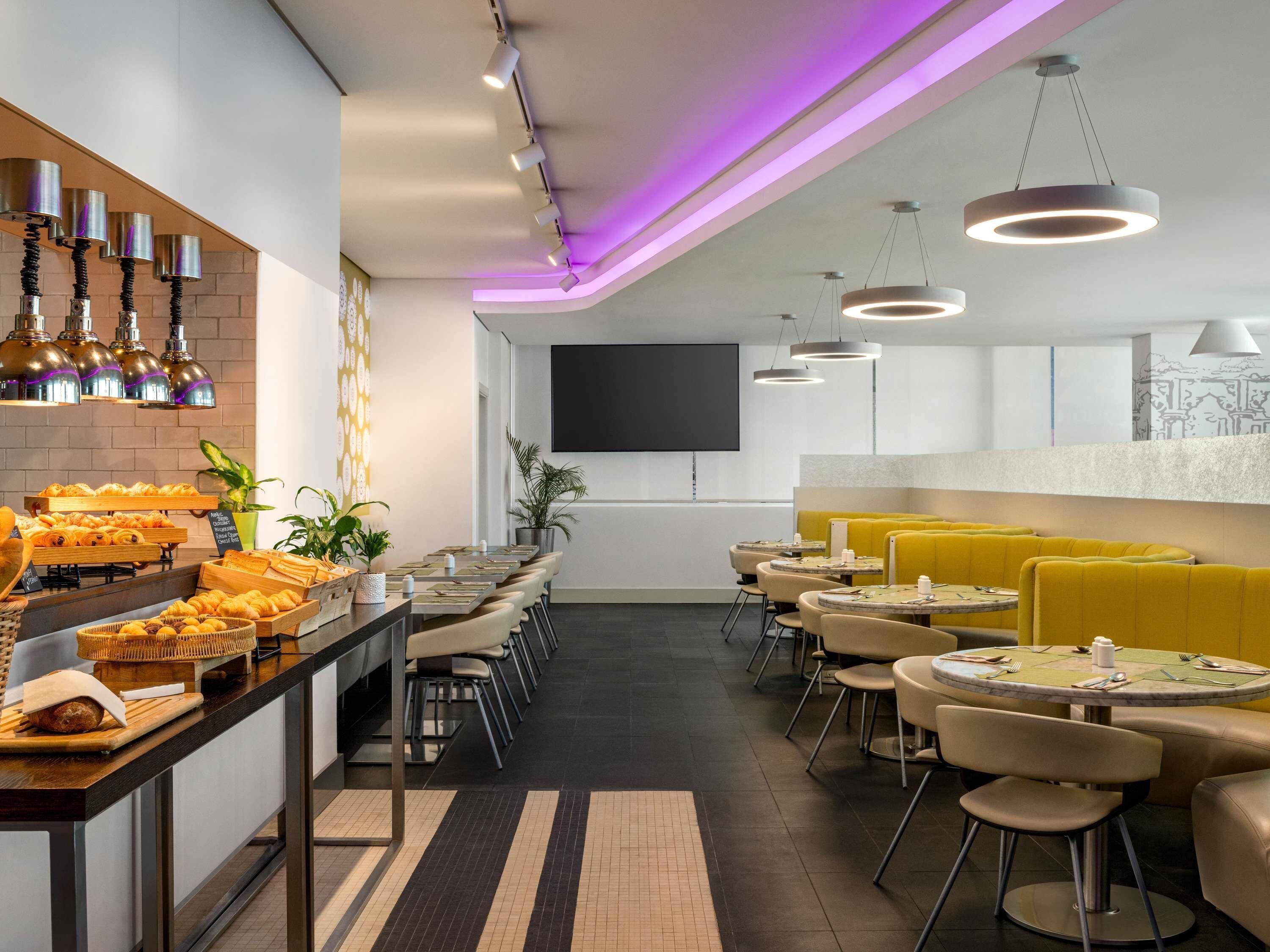 Um restaurante moderno com um balcão comprido, diversas áreas de estar e uma televisão de tela plana na parede.