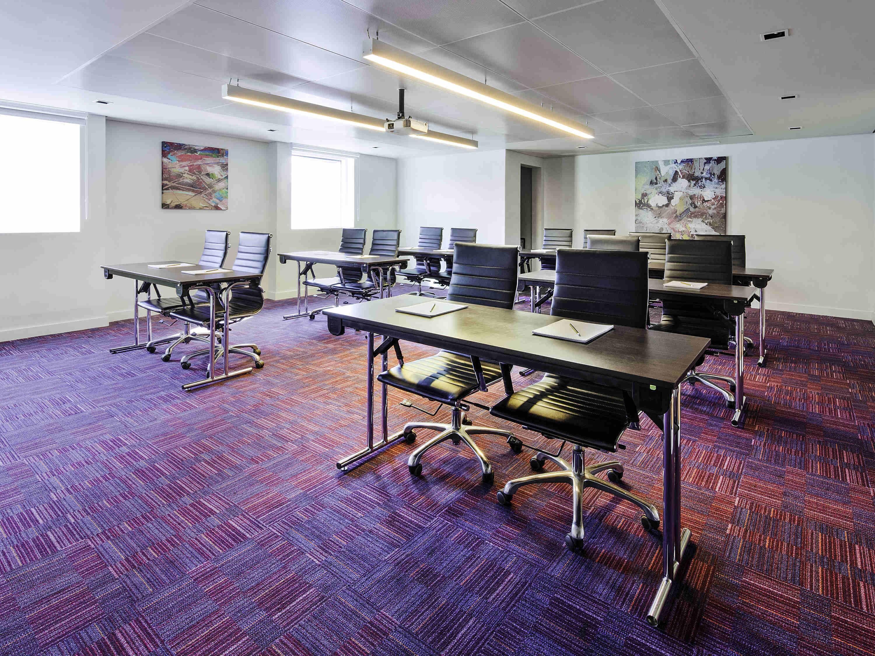 A conference room with multiple tables and chairs, a projector, and artwork on the walls.