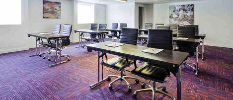 A conference room with multiple tables and chairs, a projector, and artwork on the walls.