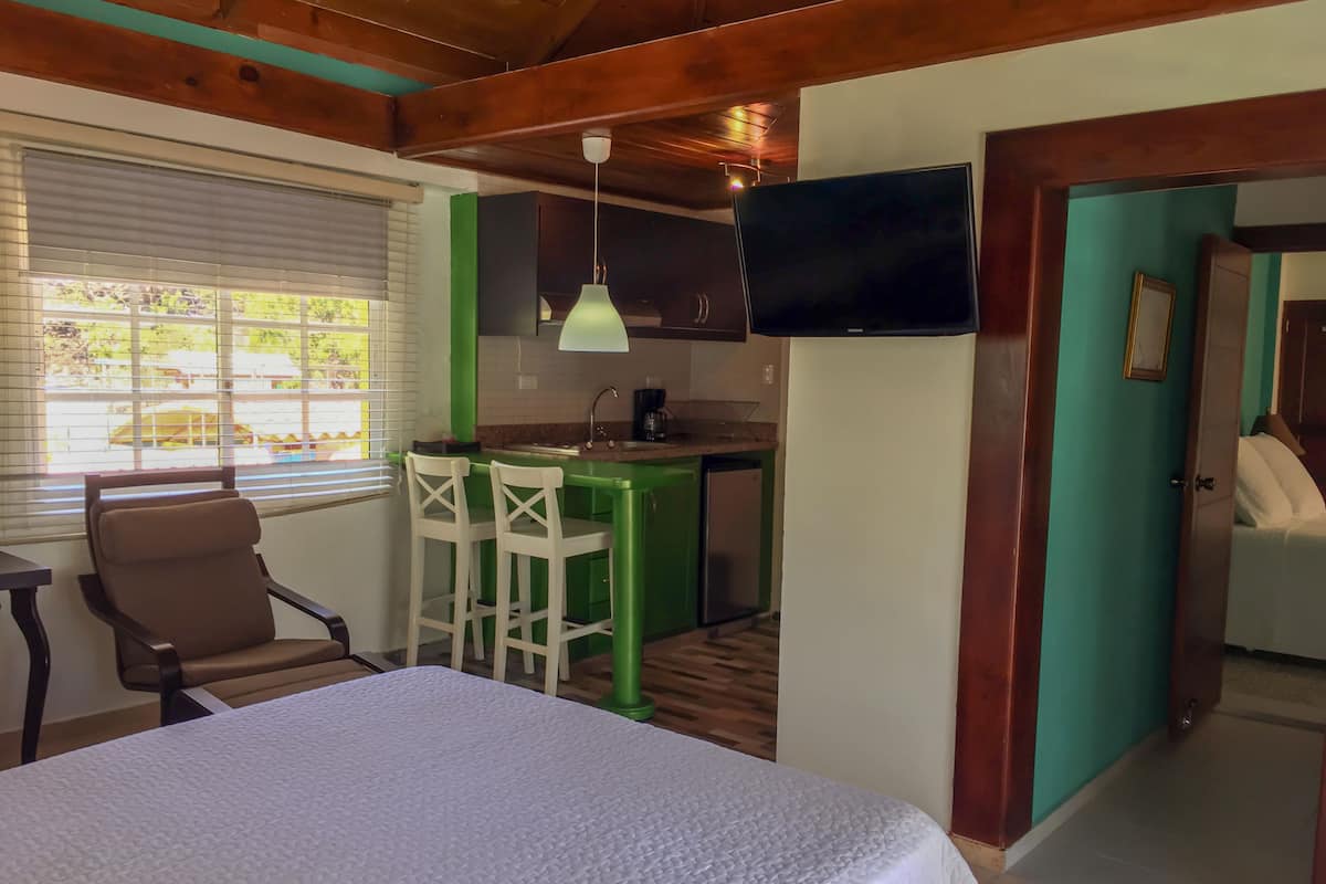 A room with a bed, a table, a green bar area, and a TV mounted on the wall.