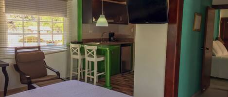 A room with a bed, a table, a green bar area, and a TV mounted on the wall.