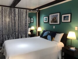 Habitación de hotel con una cama grande, dos lámparas de noche, una mesita de noche y una pared con cuadros enmarcados.