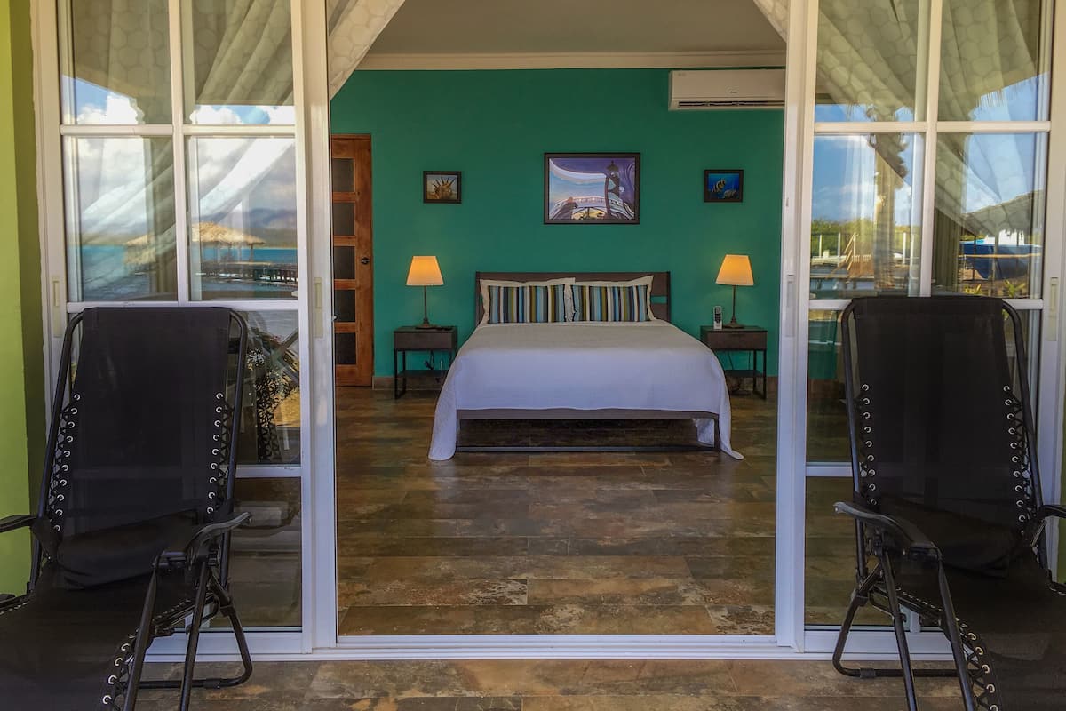 A room with a bed, two chairs, a nightstand, a lamp, and a painting on the wall.