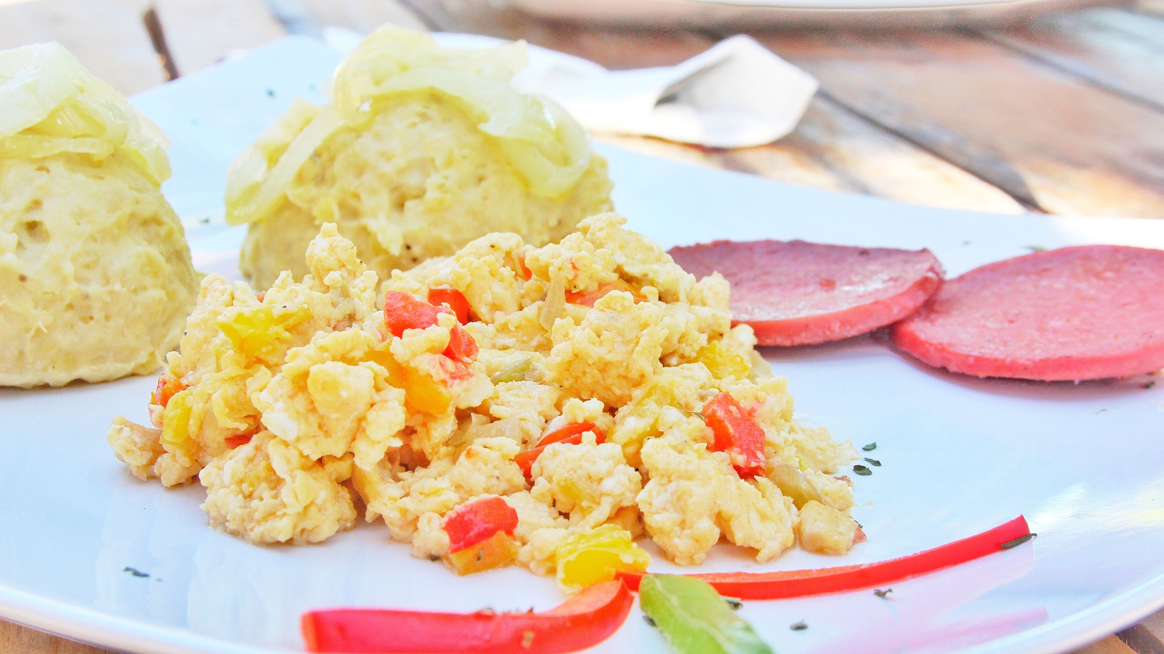 En tallrik med scrambled eggs, kåldolmar och skivad korv.